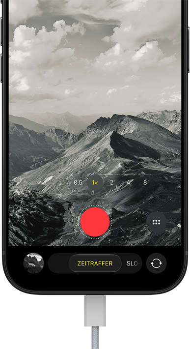 iPhone 18 Pro, Vorderseite, das Display zeigt eine Berglandschaft, mit der Kamera Modus Überlagerung im Zeitraffer Modus, mit dem Netzkabel am Ladeanschluss