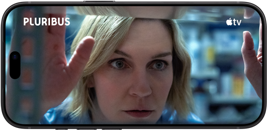 Ein iPhone 18 Pro im Querformat, das Display zeigt eine Nahaufnahme einer Frau, die aus einem Fenster schaut. Serienname: Pluribus