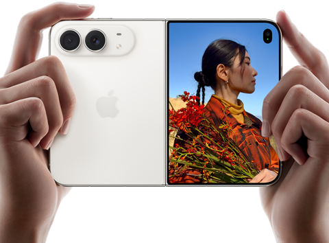 iPhone Duo, Farbe Sternenweiß, in zwei Händen im Querformat gehalten, aufgefaltet, linke Seite mit 48 MP Dual Fusion Rückkameras, rechte Seite zeigt eine Person, die fotografiert wird, auf dem äußeren Display kann die fotografierte Person während der Aufnahme mit Duo Preview ihr Gesicht sehen
