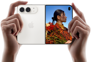 iPhone Duo, Farbe Sternenweiß, in zwei Händen im Querformat gehalten, aufgefaltet, linke Seite mit 48 MP Dual Fusion Rückkameras, rechte Seite zeigt eine Person, die fotografiert wird, auf dem äußeren Display kann die fotografierte Person während der Aufnahme mit Duo Preview ihr Gesicht sehen